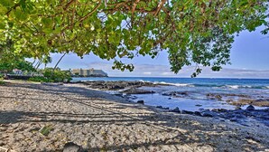 Uma praia com costa rochosa, um cruzeiro ao fundo e um edifício com telhado inclinado.