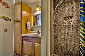 Un baño con armarios de madera, un lavamanos, un espejo y una ducha con mosaicos.