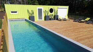 A rectangular swimming pool with a wooden deck and lounge chairs. - The Terre de feu mobile home (Châteauneuf-sur-Isère)