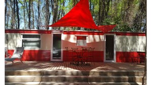 A cabin with a red and white exterior, a deck with outdoor furniture, and a large red canopy. - The Terre de feu mobile home (Châteauneuf-sur-Isère)