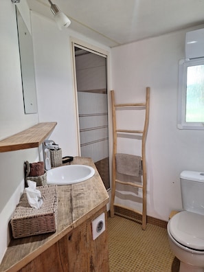 Une salle de bain avec un meuble-lavabo en bois, un lavabo blanc, un miroir, un porte-serviettes, une échelle en bois et des toilettes blanches.