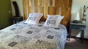 A bed with a patterned quilt, two pillows with motivational text, a wooden headboard, a nightstand with a lamp and a decorative item, and a small drawer unit. - The Terre de feu mobile home (Châteauneuf-sur-Isère)