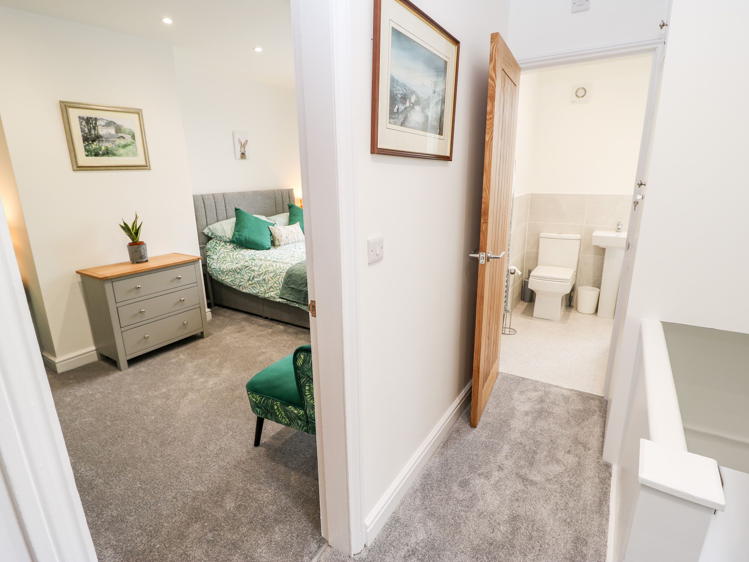 A bedroom with a bed, dresser, and a green chair. There is a bathroom with a toilet and sink.