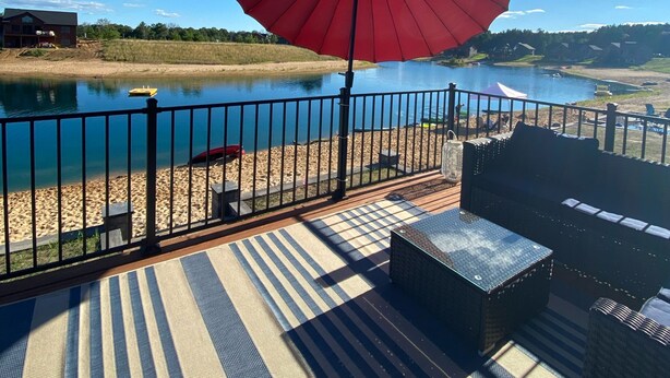 A deck with a red umbrella, a view of a lake, and a sandy beach.