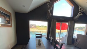 A dining area with a long table, chairs, and a view of a body of water through large windows.