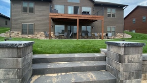 A two-story house with a balcony, stone steps, and a grassy lawn.