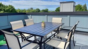 Een terras op het dak met een tafel, stoelen, een klein plantje en een functionele kast.