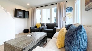 Een moderne woonkamer met een bank, twee fauteuils, een salontafel en een aan de muur bevestigde televisie.