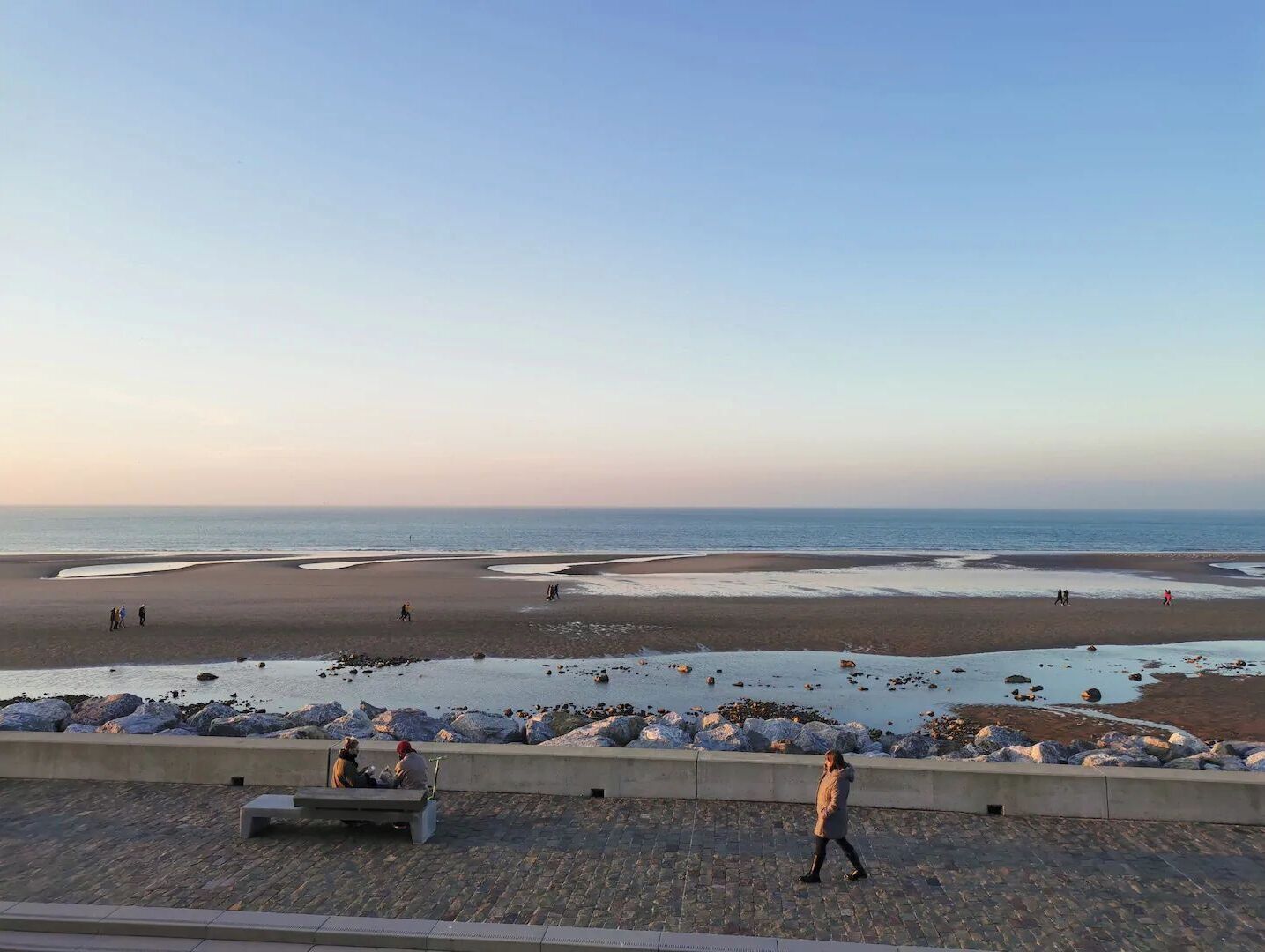 A beach with a paved walkway, benches, and a view of the sea.