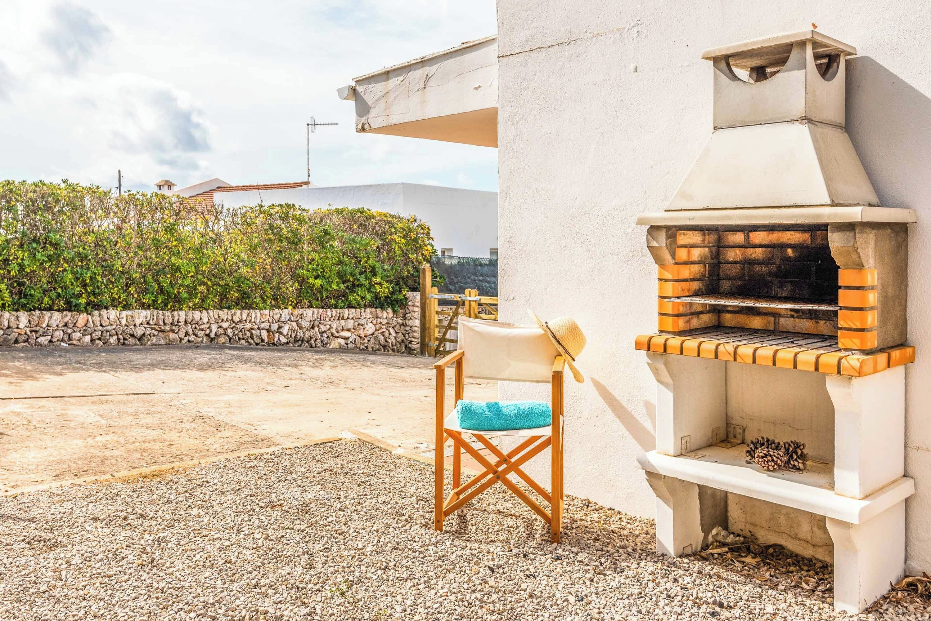 An outdoor seating area with a stone wall, a wooden chair with a blue cushion, and a brick oven grill.