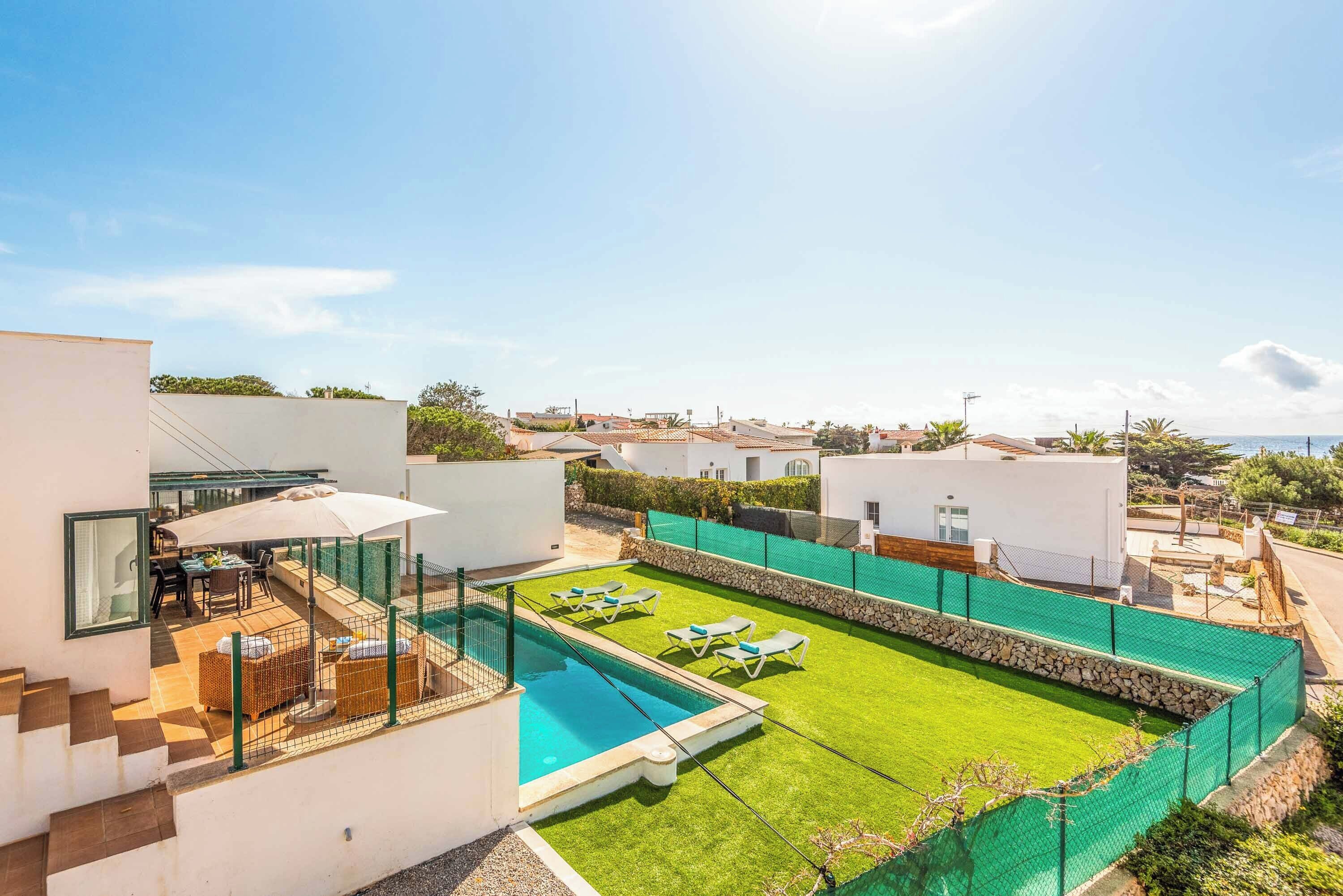 A modern villa with a swimming pool, outdoor seating, and a view of the sea.