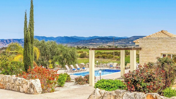 Ein Poolbereich mit Liegestühlen und einer Pergola, umgeben von Steinmauern und Grünpflanzen, mit einer Bergkulisse im Hintergrund.