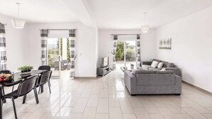 Ein modernes Wohnzimmer mit einem grauen Sofa, einem Esstisch mit Stühlen und einem TV-Schrank.