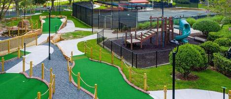 A miniature golf course with a green putting area, a play area with a slide, and a fenced walking path.