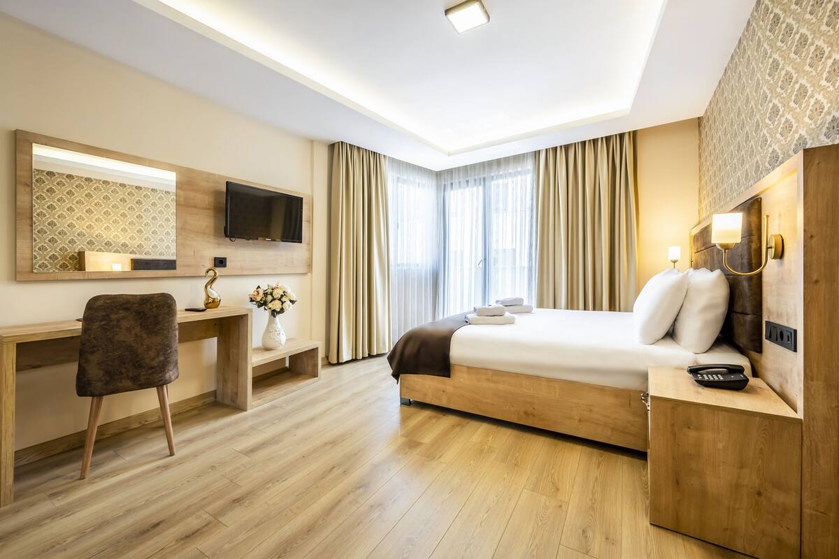 A modern hotel room with a wooden desk, a comfortable bed, a television, and a large window with curtains.