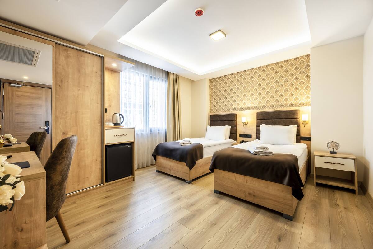 A hotel room with two beds, a desk with a chair, a small bedside table, and a wardrobe.