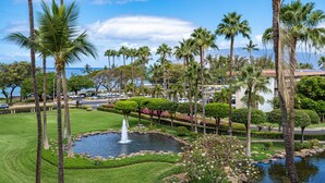 A landscaped area with palm trees, a pond, and a view of the ocean.
