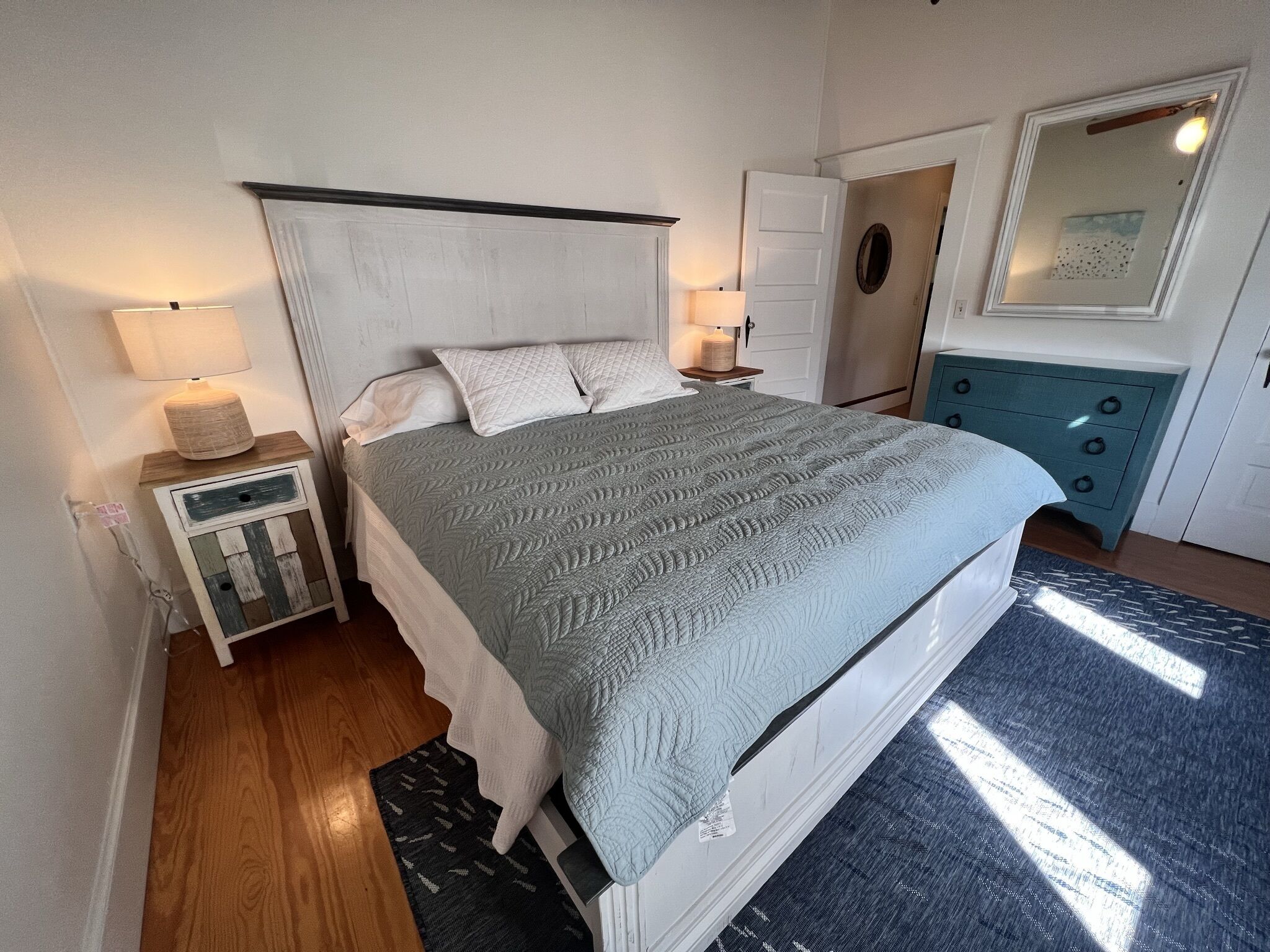 Un dormitorio con cama, mesitas de noche, cómoda, espejo y alfombra.