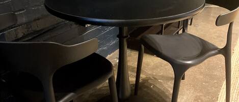 Una mesa redonda con cuatro sillas negras, frente a una pared de ladrillo oscuro.