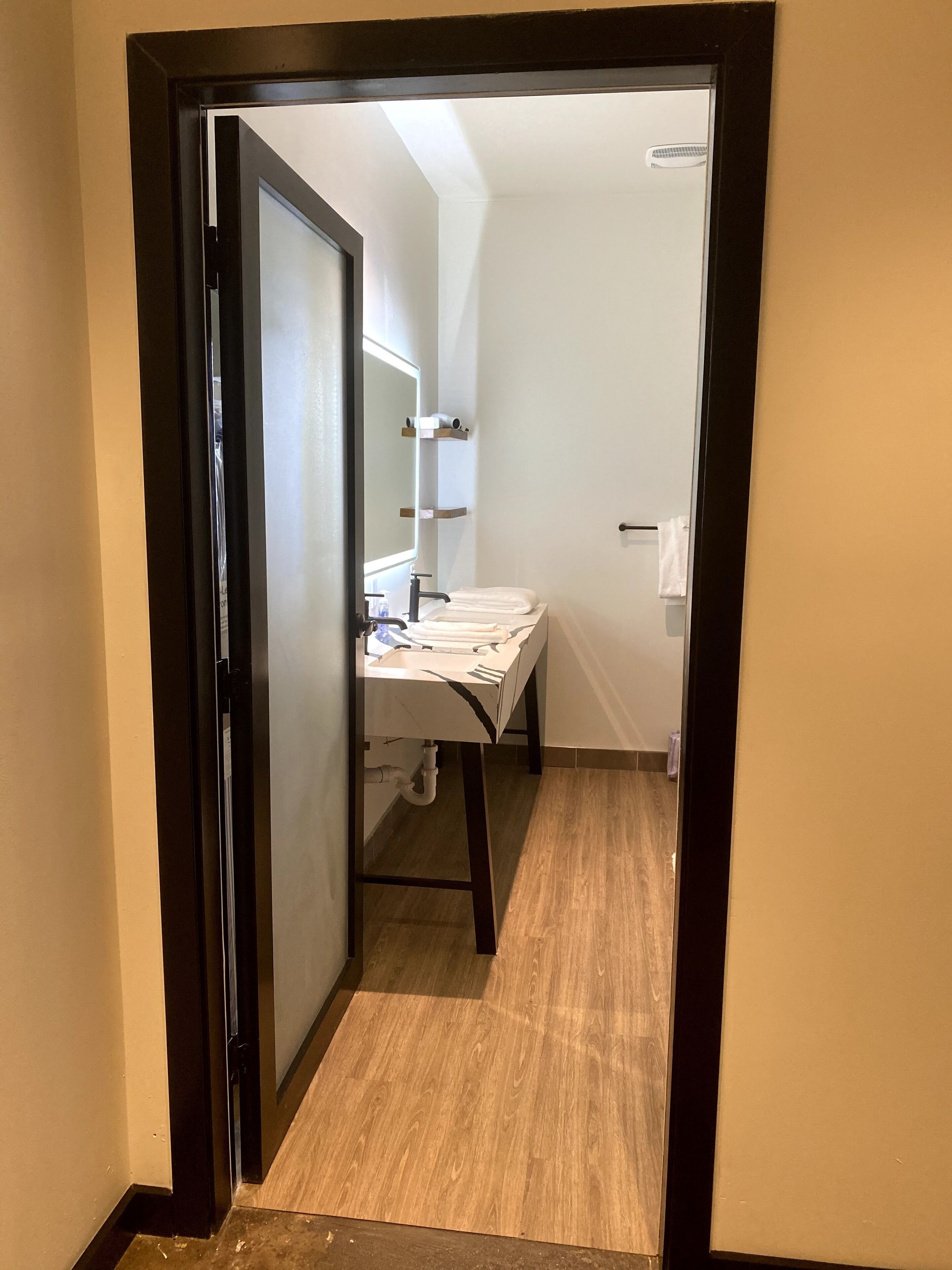 A narrow hallway leading to a bathroom with a sink, towel rack, and a mirror.