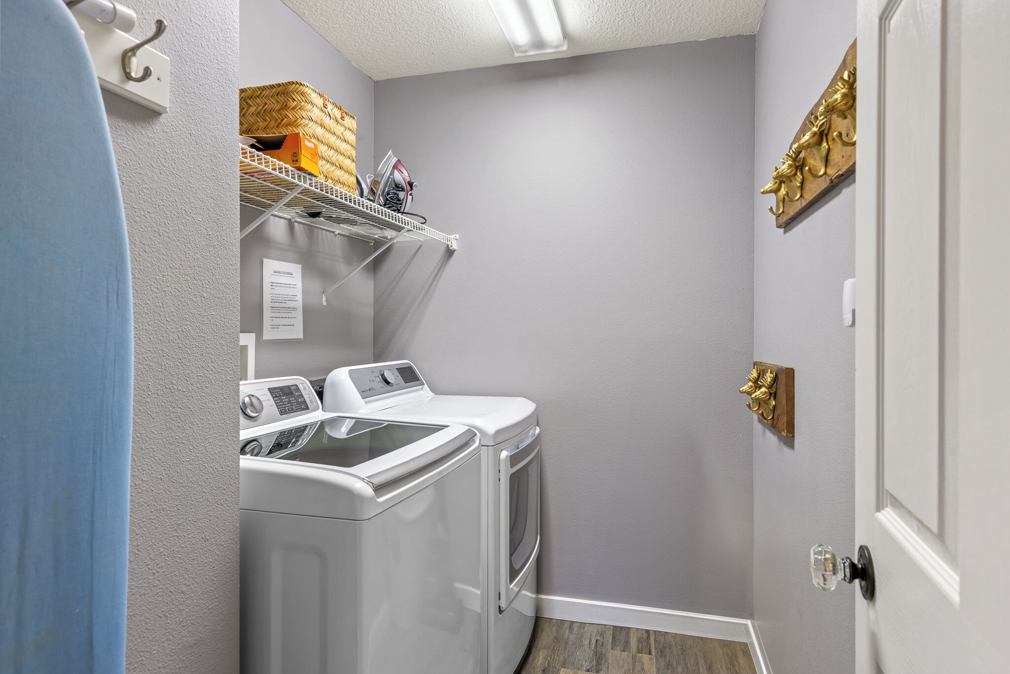 Un cuarto de lavandería con lavadora y secadora, un estante con cestas, y una placa dorada decorativa en la pared.