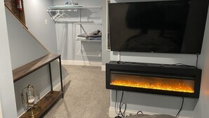 Ein Zimmer mit an der Wand montiertem Fernseher, Kamin, einem Holzkonsolentisch und einem Schrank mit Kleidung.