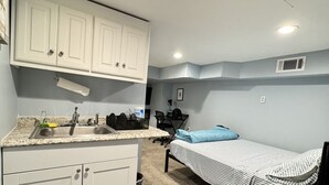 Ein kleines Zimmer mit einer Küchenzeile, einem Bett und einem Schreibtisch.