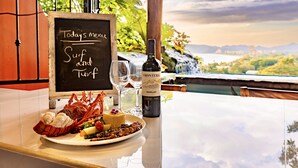 A table with a lobster dish, a bottle of wine, and a menu board with the text "Today's menu Surf and Turf". - Ocean View 🌅Infinity Pool Villa & Hot Tub !CLOSE TO BEACH! (Jaco Beach)
