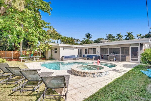 A backyard with a swimming pool, a hot tub, and a barbecue area.