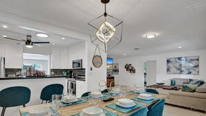 A modern kitchen with white cabinets, a central island, and a dining area set for six with blue chairs and a wooden table.