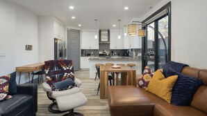 A modern living room with a leather sofa, a cushioned chair, and a dining area with a wooden table. - Downtown Retreat | Steps to Bike Path &Restaurants (Moab)