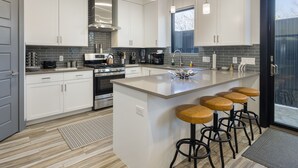 A modern kitchen with white cabinets, a stainless steel stove, and a large island with bar stools. - Downtown Retreat | Steps to Bike Path &Restaurants (Moab)
