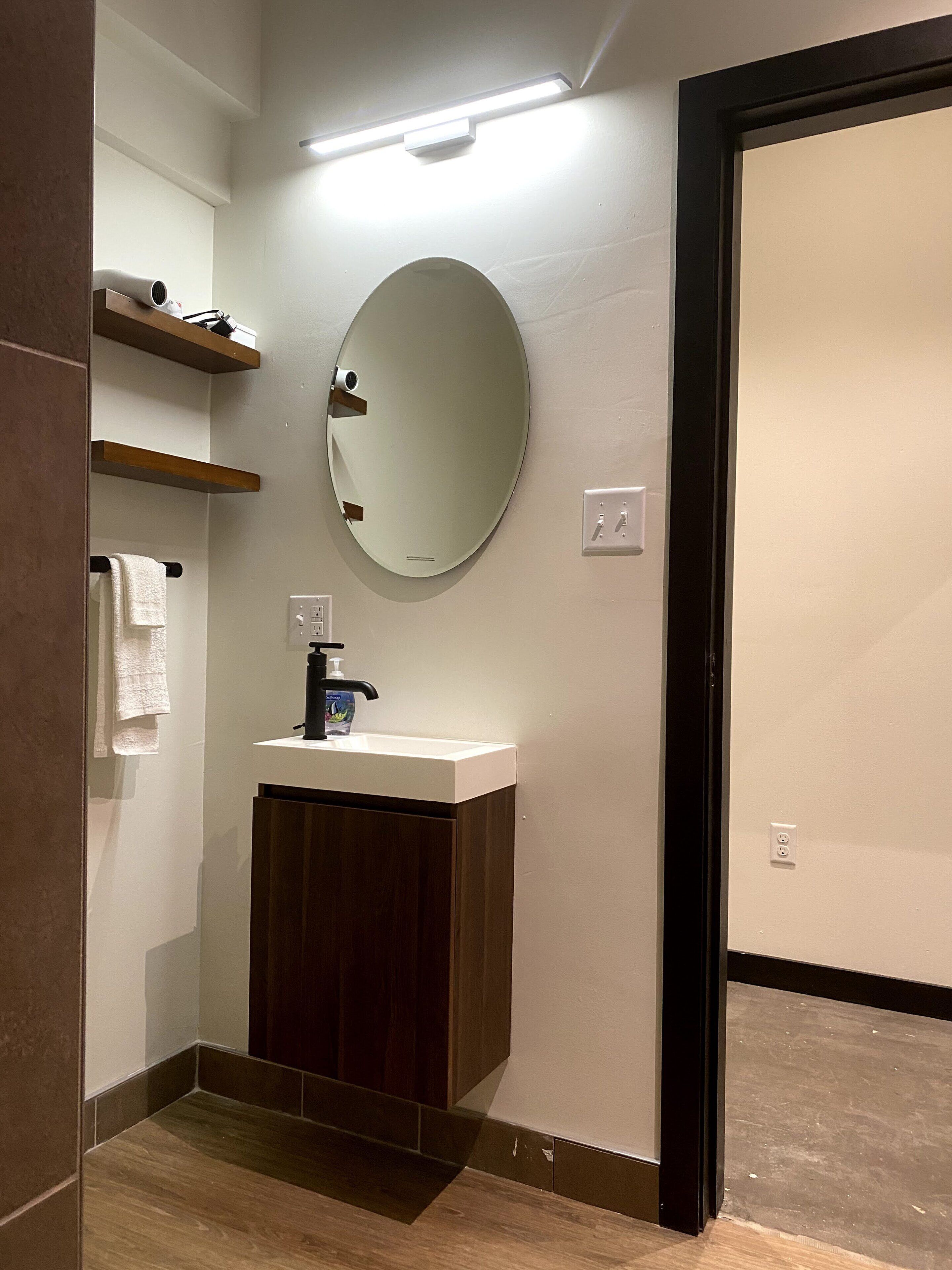 A modern bathroom with a round mirror, a white sink, and wooden cabinets.