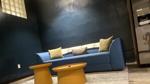 En moderne stue med en blå sofa, to gule sofaborde og en gulvtæppe med et mønster.