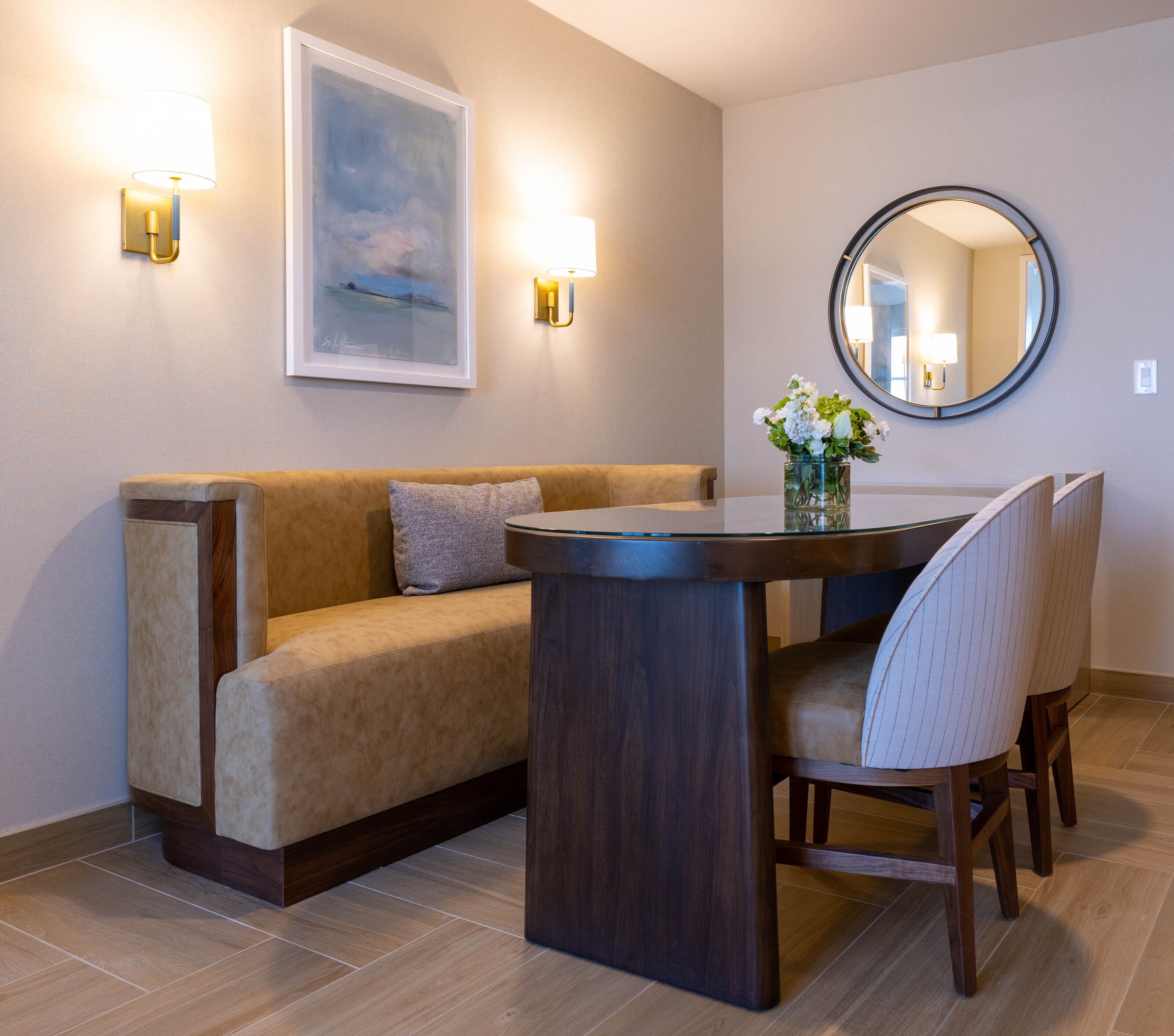 A modern dining area with a glass-top table, cushioned seating, and wall-mounted lighting.