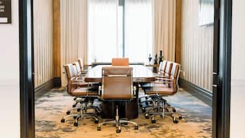 A conference room with a large table and six chairs, a carpeted floor, and a view through a glass door.