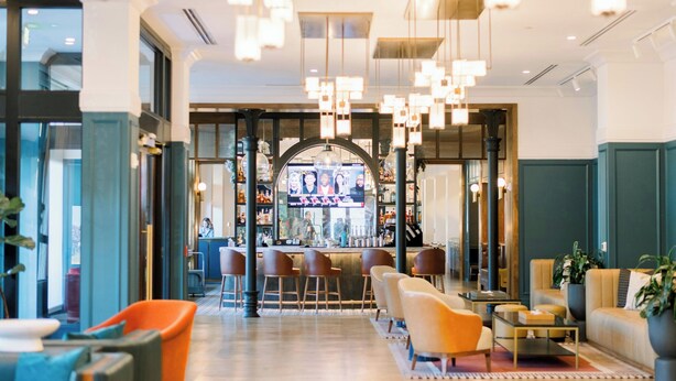 A modern lobby with a bar area, seating, and a television screen.