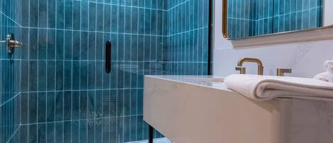 A modern bathroom with a glass shower enclosure, a vanity with a mirror, and a white towel on the counter.