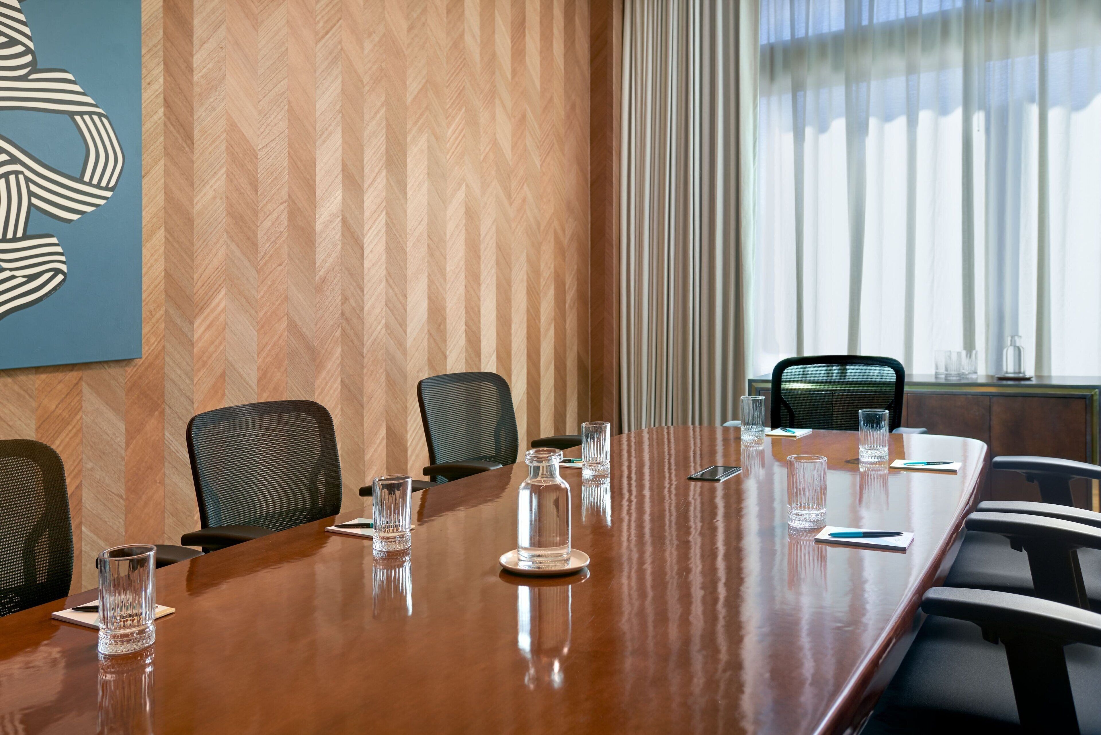 Une salle de conférence avec une longue table en bois, plusieurs chaises et de la verrerie.