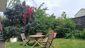 Eine Terrasse mit einem Holztisch und vier Stühlen, umgeben von üppiger Vegetation und blühenden Bäumen.