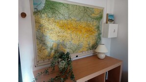 Eine große Karte an der Wand, eine kleine Lampe auf einem Holztisch und ein Buch mit dem Titel 'Les Pirenées'.