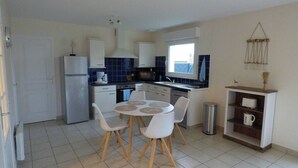 A compact kitchen with white cabinets, a built-in oven, a sink, and a dining area with a round table and chairs.