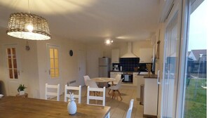 A modern kitchen with white cabinets, a dining area with a wooden table and white chairs, and a large window offering a view of the outdoors.