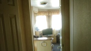 A narrow hallway leading to a kitchen area with a refrigerator, a sink, and a window with curtains.