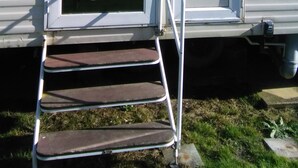 A mobile home with a sliding door, a small set of steps leading to the door, and a window on the side.