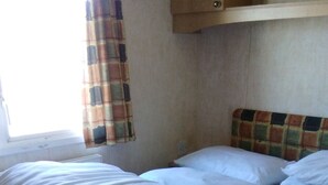A single bed with white bedding in a room with a window and a curtain.