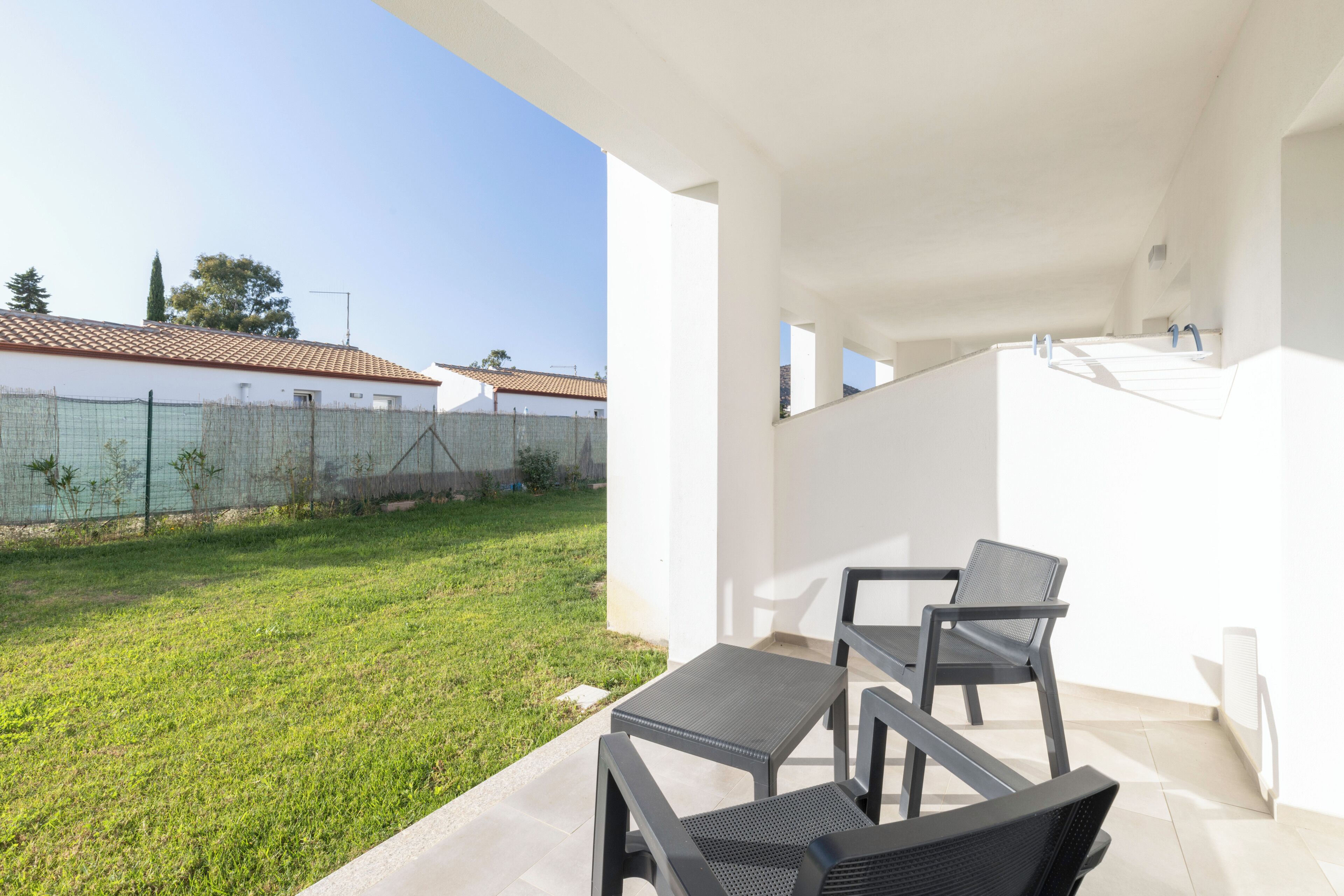 Un patio con una mesa y sillas, un jardín con césped y un edificio blanco con techo de tejas al fondo.