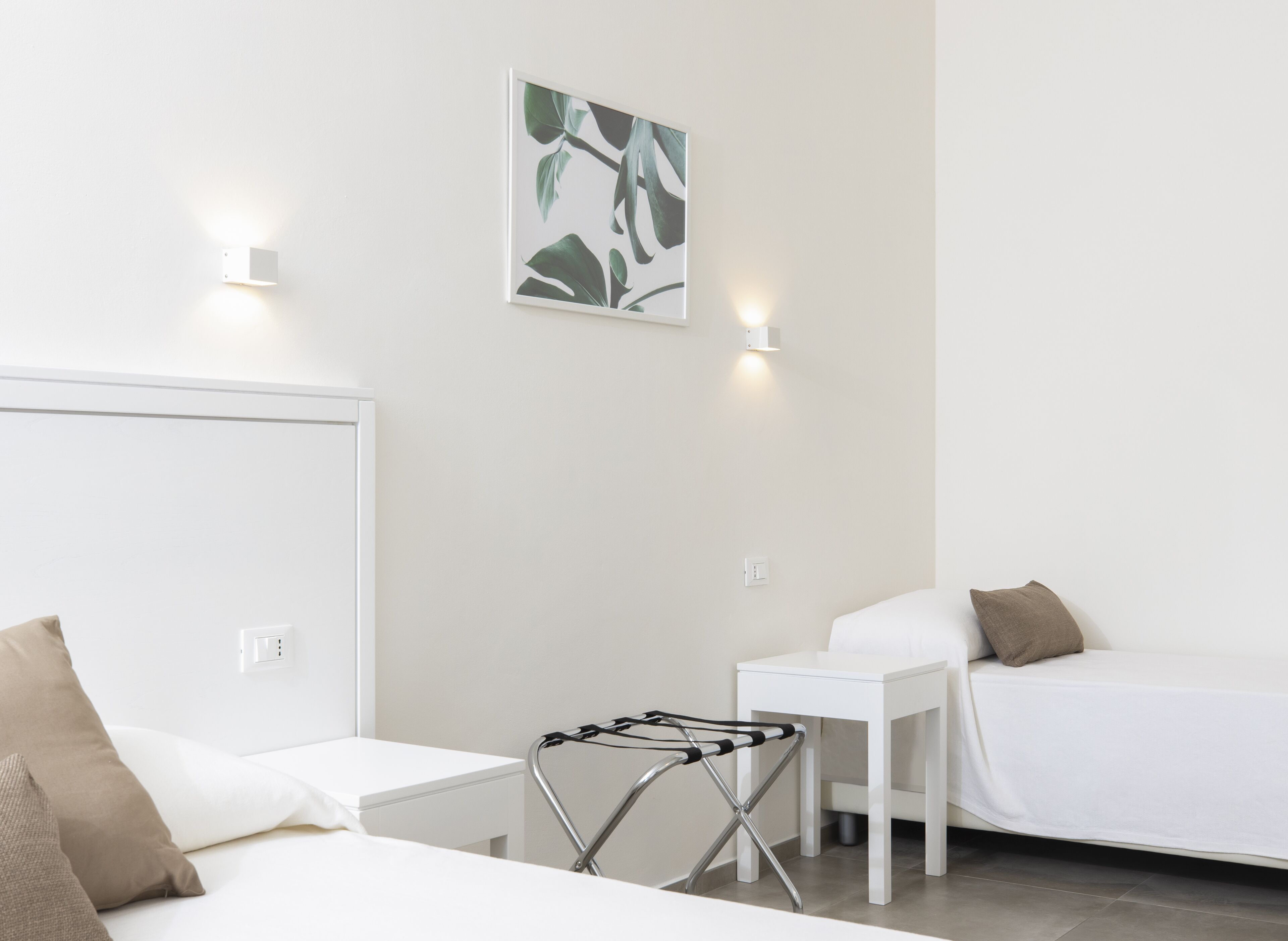 Une chambre d’hôtel avec deux lits, une petite table, une lampe fixée au mur et une plante fixée au mur.