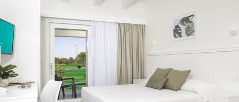 A bedroom with a bed, a desk, a chair, and a view of a green landscape through a door.