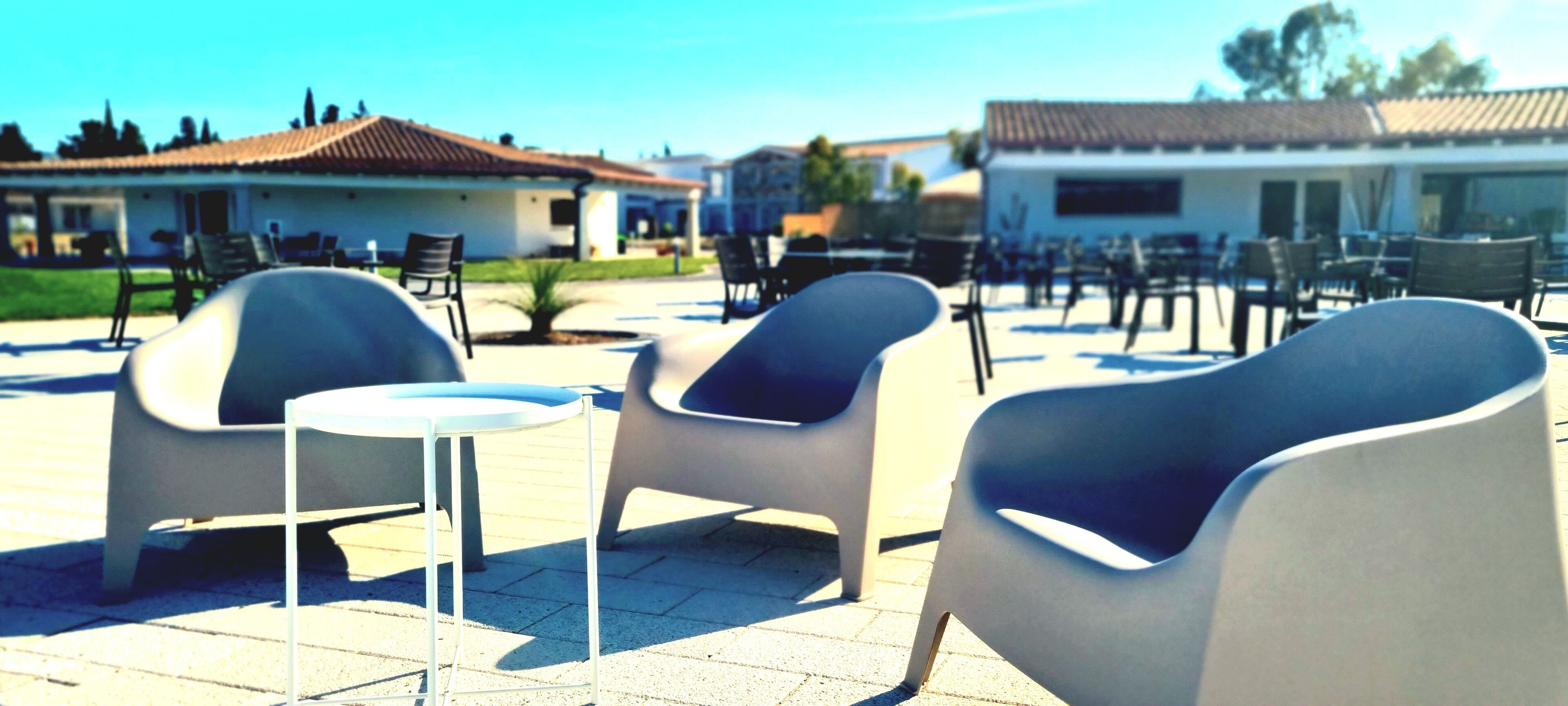 A patio area with modern chairs and tables, a small round table, and a building with a tiled roof in the background.